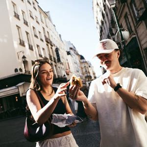Travellers enjoying a French pastry while exploring a charming street on the Contiki France in a Week Tour