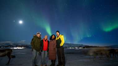 Four travellers stood in front of the northern lights in Tromso, Norway