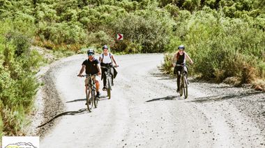 Three travellers each riding a mountain bike on a dirt road in the Swartberg mountains, South Africa