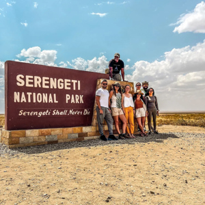 Group of travellers standing next to the entrance sign to the Serengeti National Park, Tanzania
