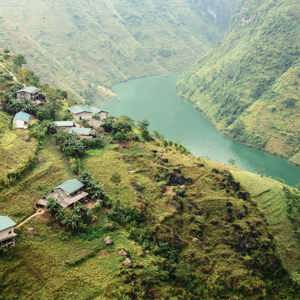 A winding emerald river curves through the mountains of northern Vietnam, with small rural villages and terraced hillsides overlooking the Ha Giang Loop - Northern Vietnam Tour