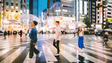 Three Travellers Walking Across Shibuya Pedestrian Crossing at Dusk with Umbrellas, Tokyo, Japan