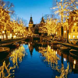 Golden Christmas fairy lights reflecting in an Amsterdam canal at night with the Rijksmuseum in the background - Contiki Amsterdam Christmas Tour