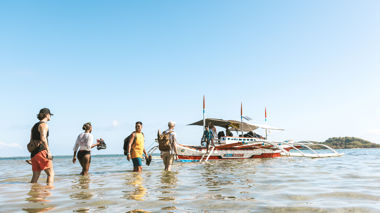 Travellers walking out to a boat in shallow water in Moalboal, Philippines