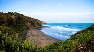 Black sand beach, green cliffs and blue ocean water, Muriwai, New Zealand