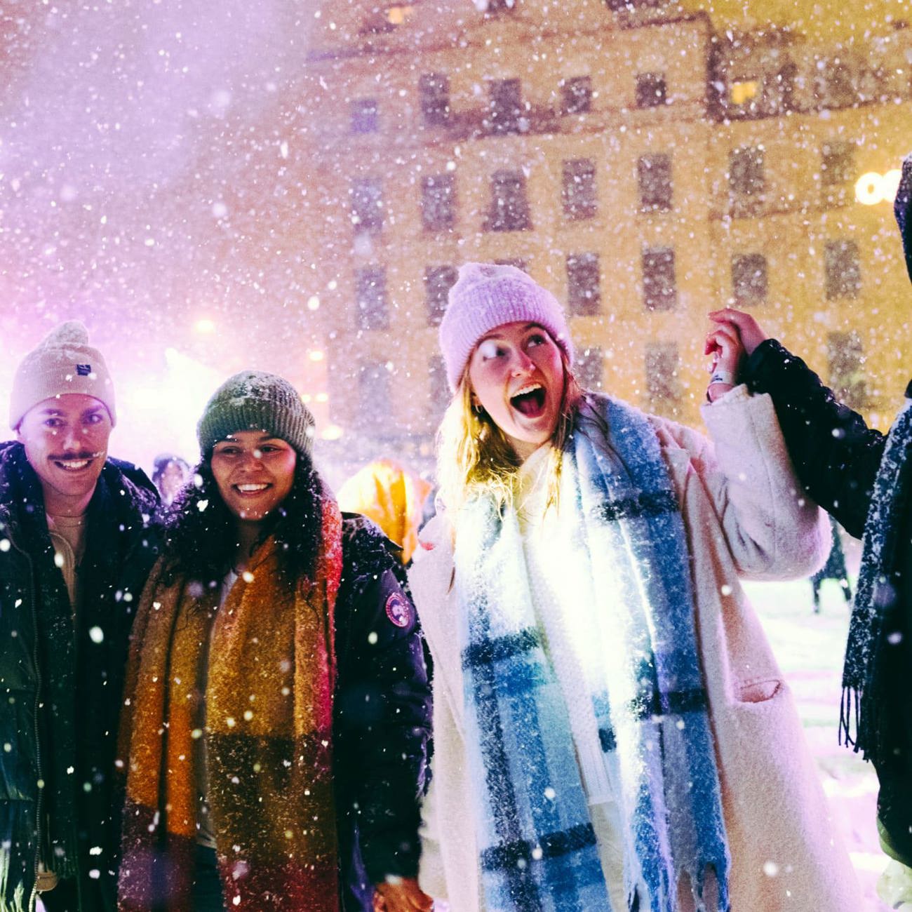 Group of four young travellers laughing in the snow at a festive Christmas market at night - Contiki German Christmas Markets Tour