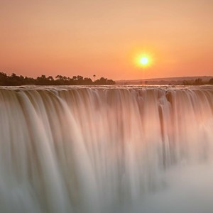 A waterfall flowing at sunset beneath an orange sky in Zimbabwe