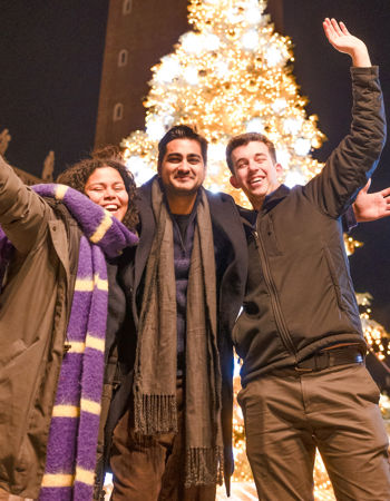 Three travellers dressed warmly standing in front of a Christmas Tree