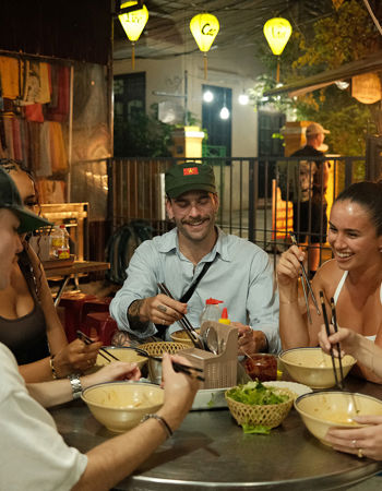 Friends laughing, eating food at a night market, Hoi An, Vietnam