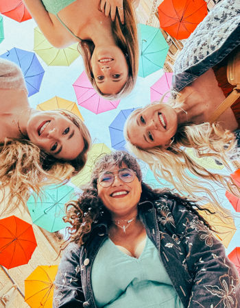 Four travellers looking down into the camera under colourful umbrellas in Barcelona, Spain