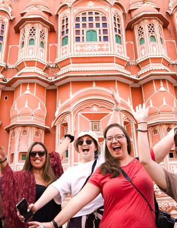 Five happy travellers standing with their arms up in the air in front of a local building in Delhi, India