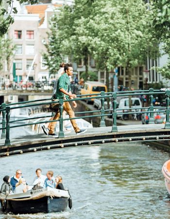 Travellers crossing a bridge over a boat in the canals of Amsterdam, Netherlands