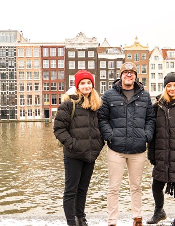 Travellers stood in front of a canal and gable houses during winter in Amsterdam, Netherlands