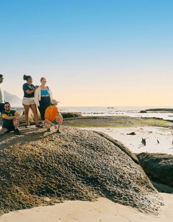 Travellers sitting on a boulder, admiring the penguins at Boulder Beach in Cape Town, South Africa