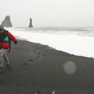Traveller walks along Reynisfjara Black Sand Beach with the Reynisdrangar sea stacks in Iceland on the Contiki Best of Iceland Tour