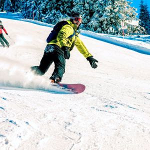 A snowboarder carves down a snowy slope in the Austrian Alps, with skiers following behind on a clear winter day