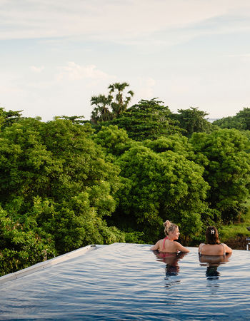 Two travellers looking at trees whilst in an infinity pool in Sanur, Indonesia