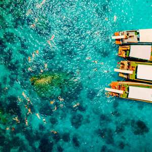 Contiki travellers swimming and snorkelling in vivid turquoise waters around traditional wooden boats anchored off the coast of a Thai island on a Thai Island Hopping East Tour