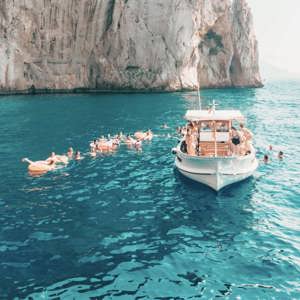 Travellers swim from a boat in the turquoise waters off the coast of Capri on the Contiki Best of Italy Tour