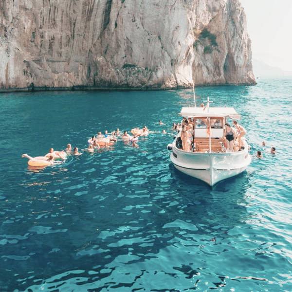 Travellers swim from a boat in the turquoise waters off the coast of Capri on the Contiki Best of Italy Tour