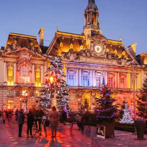 Contiki travellers exploring a stunning Christmas market square in Paris with a illuminated baroque town hall and decorated Christmas trees at twilight