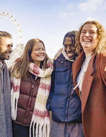 Four travellers hugging and smiling with the London Eye in the background, London, England