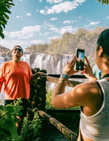 Traveller taking a photo of friend stood at view point overlooking Victoria Falls, Zambia