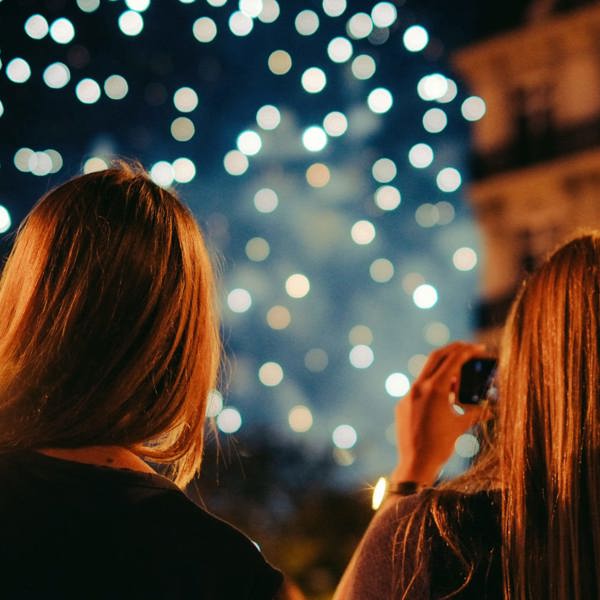 Two young women photographing New Year's Eve fireworks display in Paris France at night - Contiki Paris New Year's Eve Tour