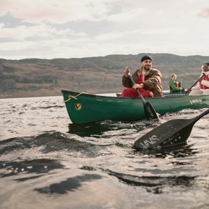 Contiki Travellers explore the Scottish Highlands by canoe, paddling across a tranquil loch with rolling hills in the background - Best of England & Scotland Summer Tour
