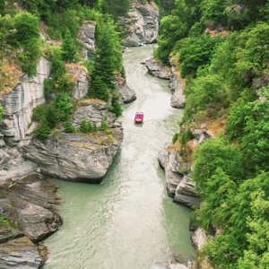 Red jet boat navigating the narrow Shotover River Canyon gorge near Queenstown New Zealand - Contiki NZ Tour