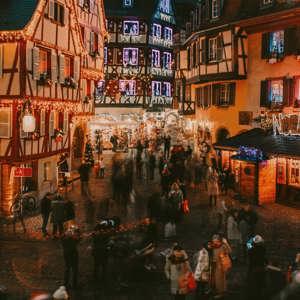 Travellers explore a festive Christmas market surrounded by illuminated half-timbered buildings in France on the Contiki French Christmas Markets Tour