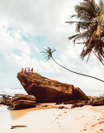 Travellers sitting on a rock on a golden beach in Koh Samui, Thailand