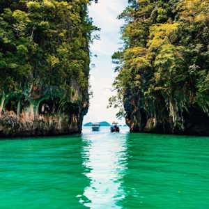 Longtail boats between towering limestone cliffs in the emerald waters of Phang Nga Bay Thailand - Contiki Thai Island Hopping West