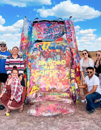 Travellers posing in front of a car at Cadillac Ranch in Amarillo, USA
