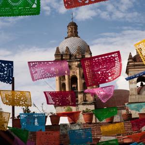 Colourful papel picado banners hanging above a colonial Mexican street with a baroque church dome and bell tower in Oaxaca Mexico - Contiki Mexico Tour